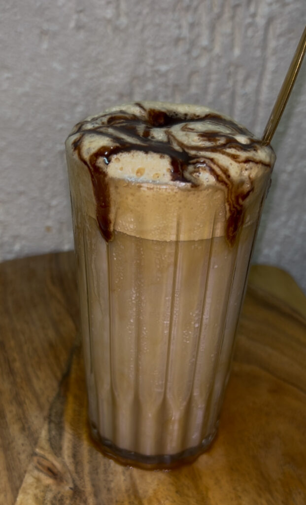 Glass of homemade iced coffee with ice cubes and a straw on a summer day