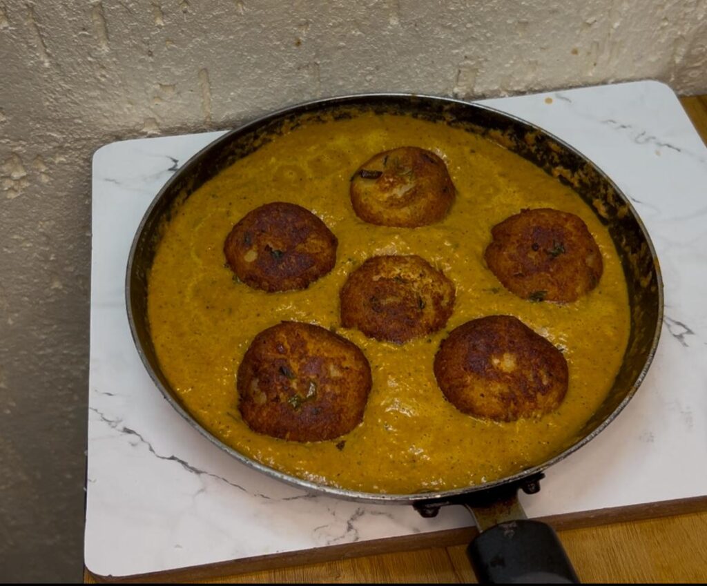 Spoonful of creamy tofu curry being served from a one-pot dish